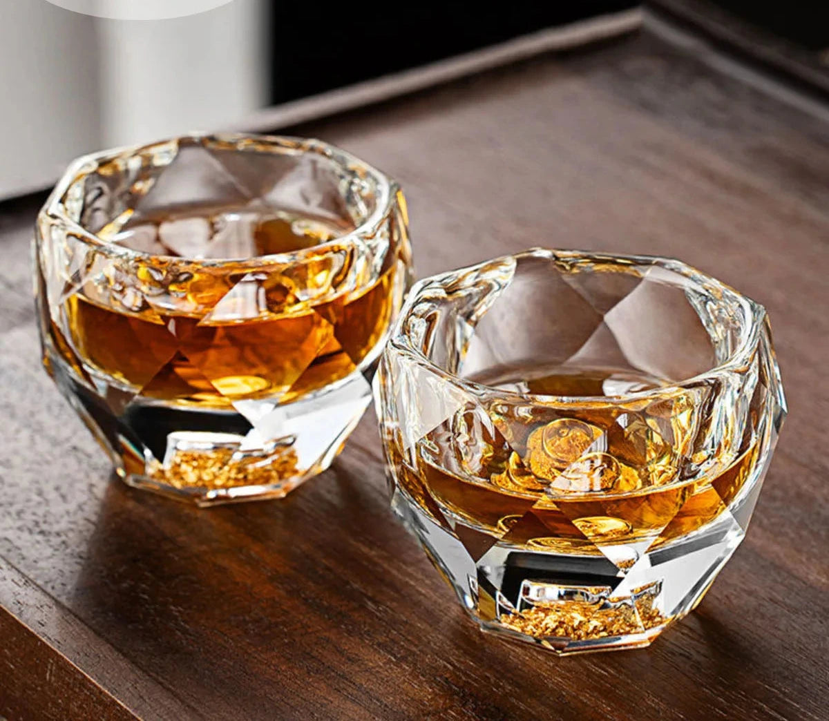 Two faceted crystal shot glasses with whiskey on a wood table